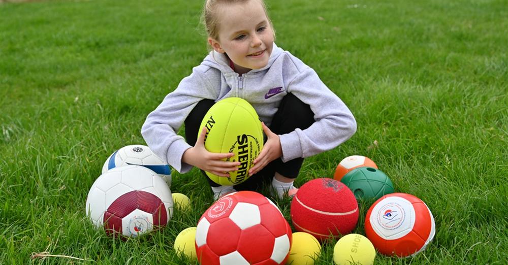 Young blind girl playing with a range of sports balls including AFL, soccer, tennis and netball